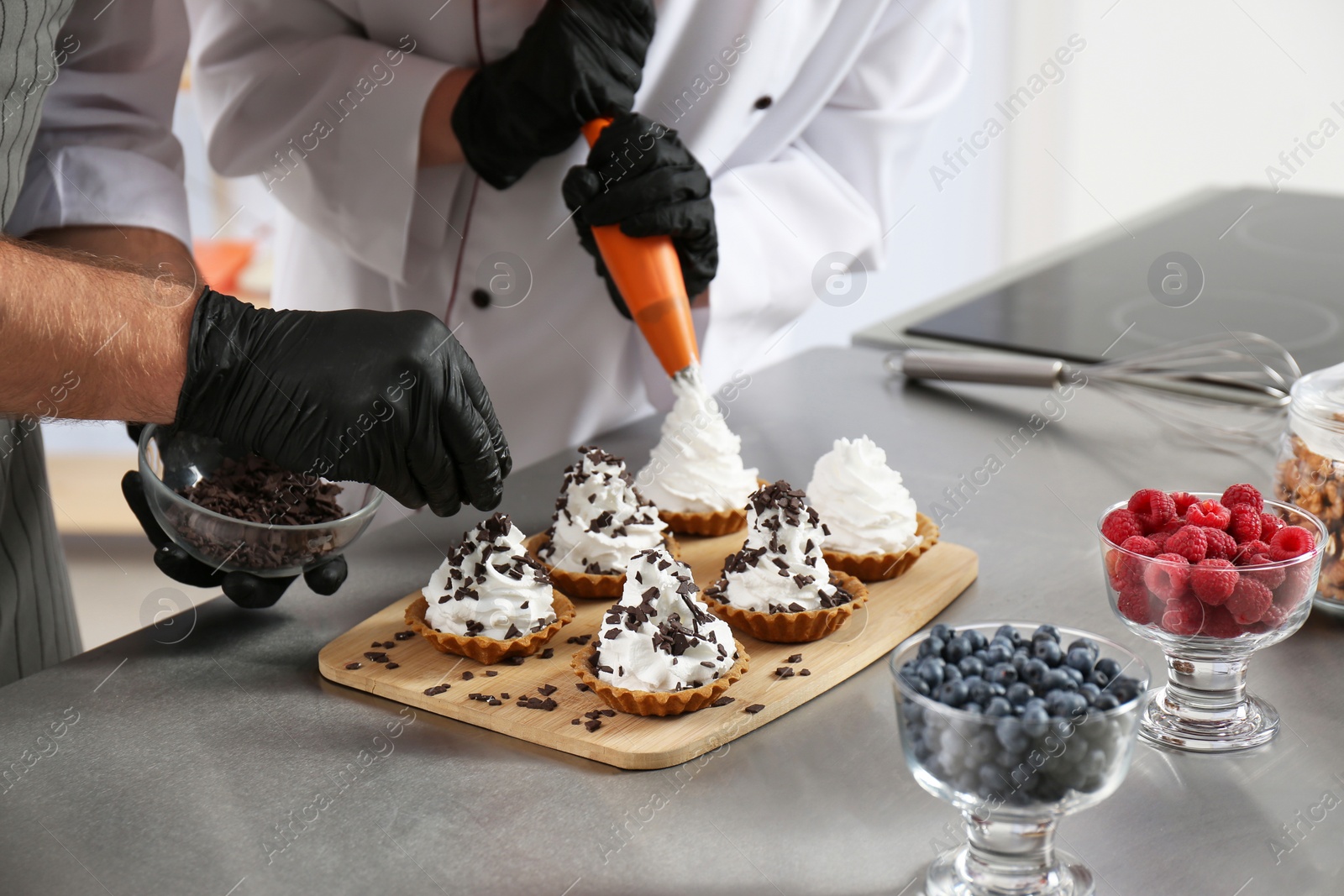 Photo of Pastry chefs preparing desserts at table in kitchen, closeup