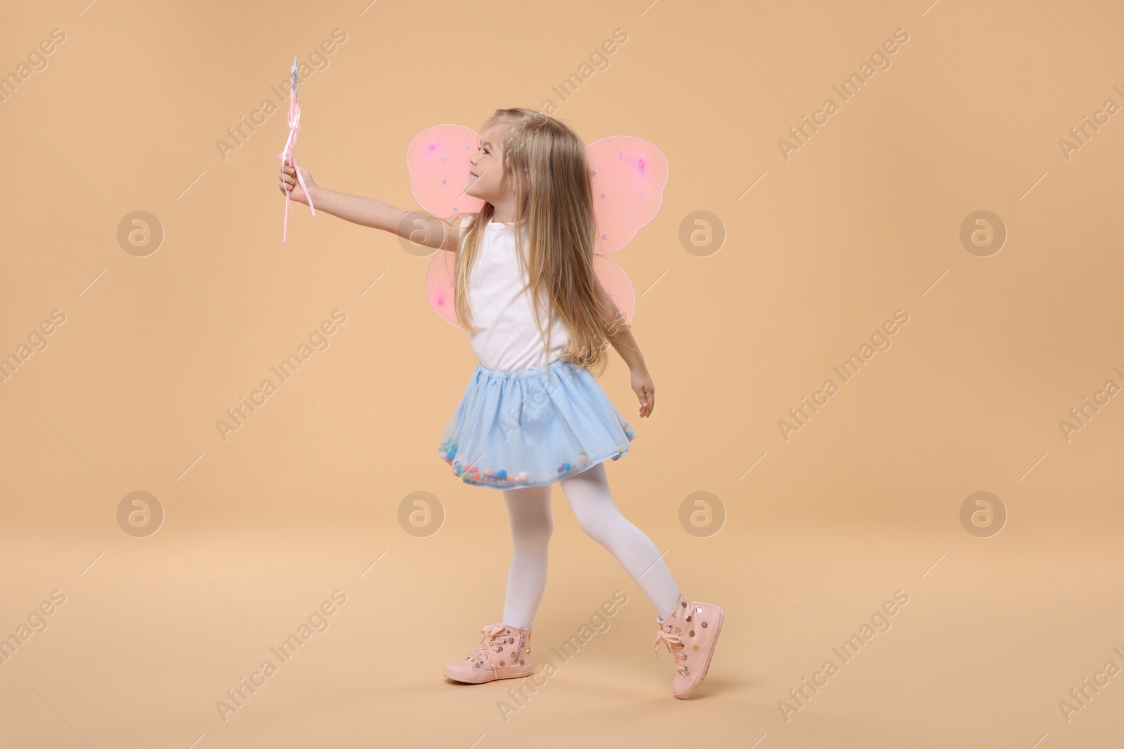 Photo of Cute little girl in fairy costume with pink wings and magic wand on beige background