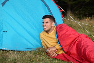 Man in sleeping bag near camping tent outdoors