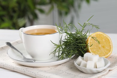 Photo of Aromatic herbal tea, fresh tarragon sprigs, sugar cubes and lemon on white table, closeup