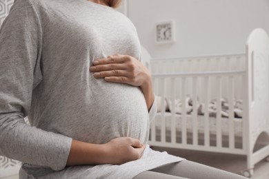 Pregnant woman in baby room, closeup view. Space for text