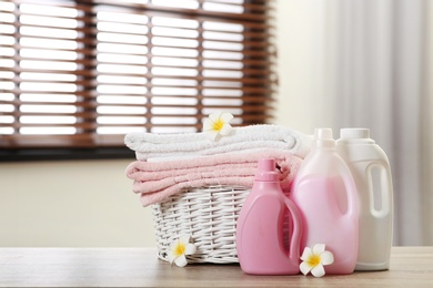 Photo of Clean towels in basket with flowers and detergents on table indoors. Space for text