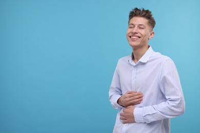 Young man laughing on light blue background. Space for text