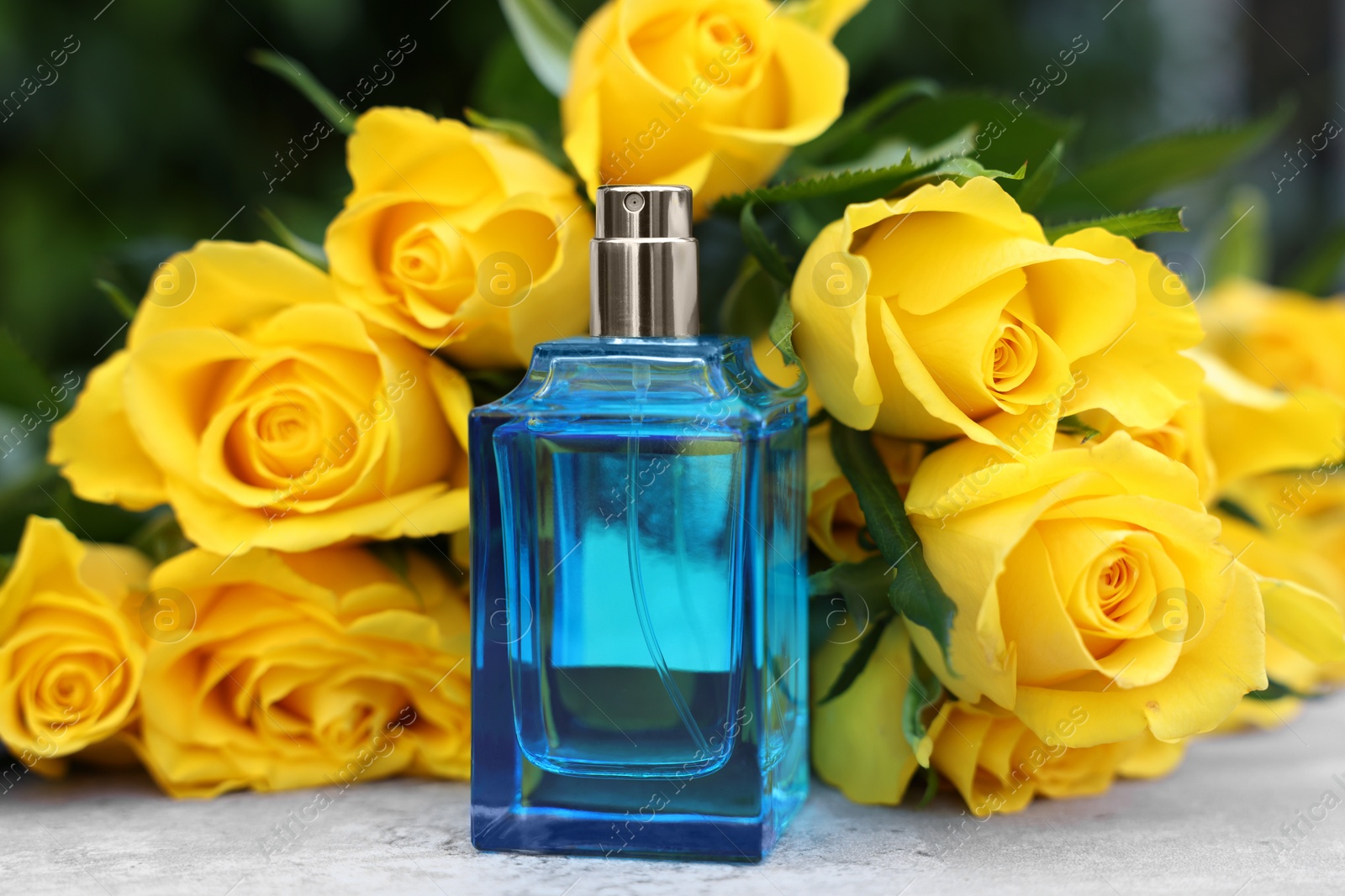 Photo of Perfume and beautiful bouquet of yellow roses on light table, closeup