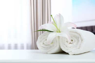 Photo of Rolled towels and flower on table in bedroom. Space for text