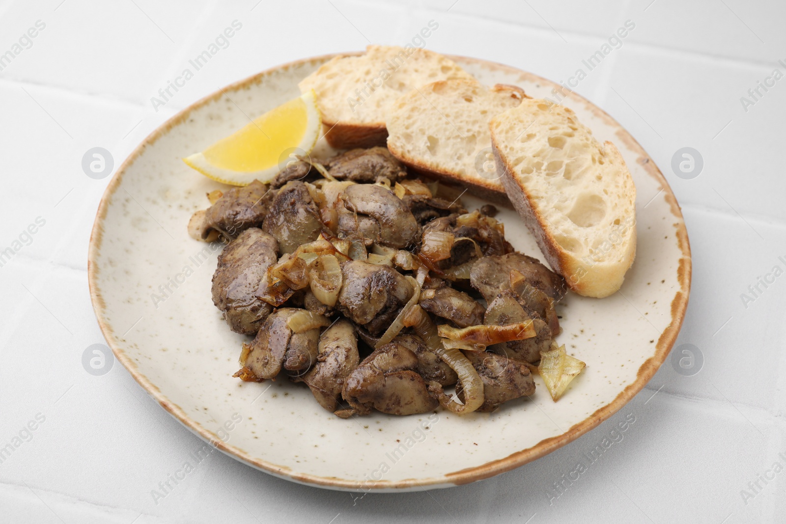 Photo of Tasty fried chicken liver served with lemon and bread on white tiled table, closeup