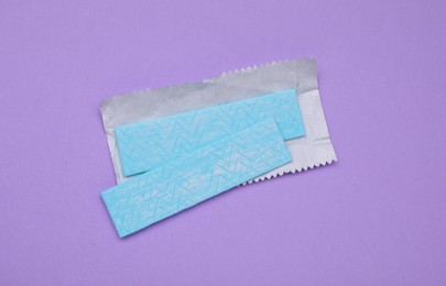 Photo of Sticks of tasty chewing gum on violet background, flat lay
