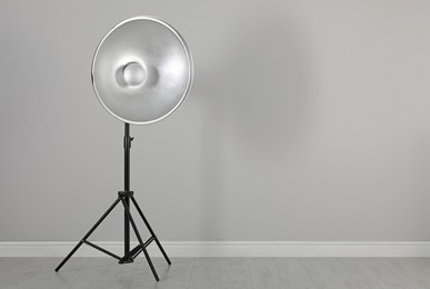 Photo of Professional beauty dish reflector on tripod near grey wall in room, space for text. Photography equipment