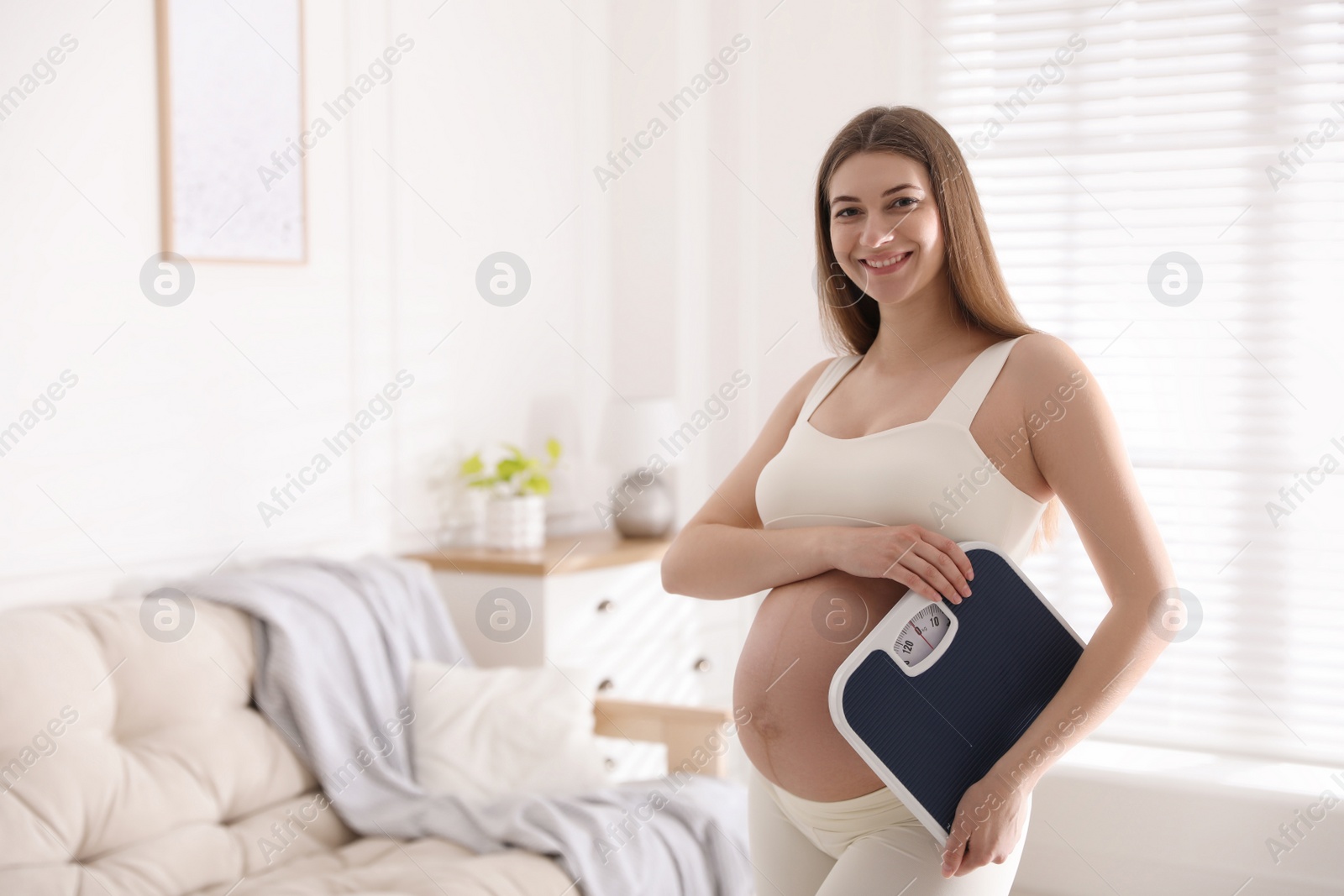 Photo of Young pregnant woman with scales at home. Space for text