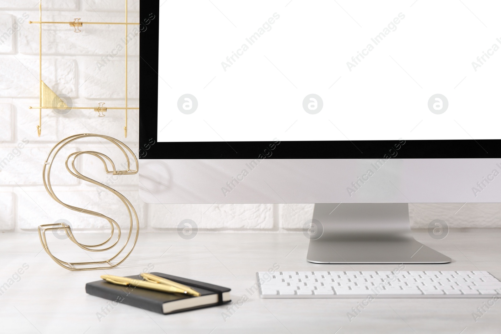 Photo of Office workplace with computer, stationery and decor on light table near white brick wall