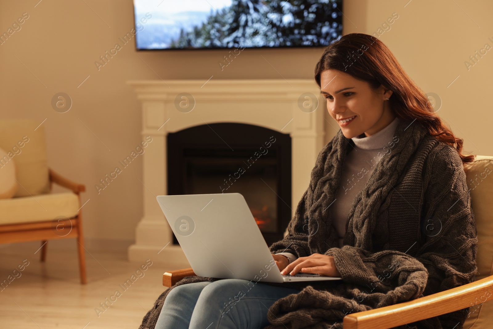 Photo of Young woman working on laptop near fireplace at home