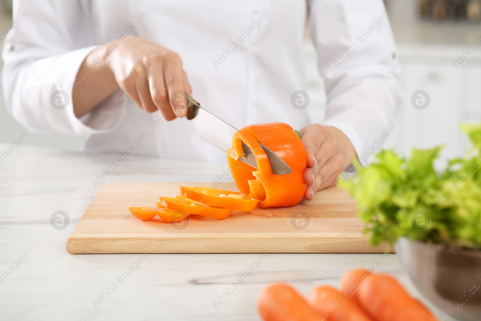 Photo of Professional chef cutting cut bell pepper at white marble table in kitchen, closeup
