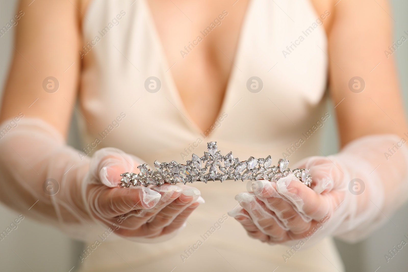 Photo of Bride holding luxurious tiara on grey background, closeup view