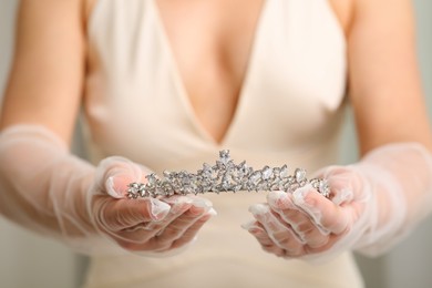 Bride holding luxurious tiara on grey background, closeup view