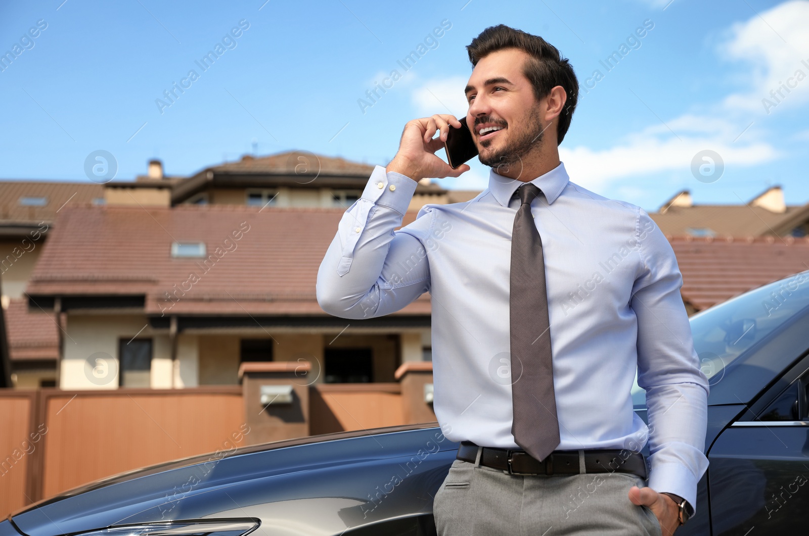 Photo of Attractive young man talking on phone near luxury car outdoors