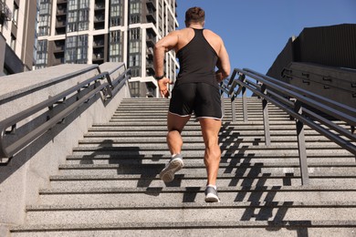 Photo of Man running up stairs outdoors on sunny day, back view