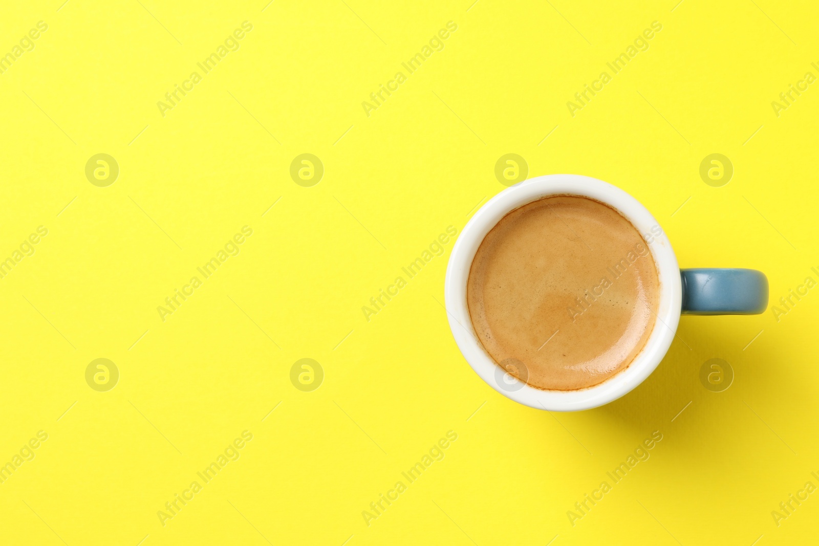 Photo of Aromatic coffee in cup on yellow background, top view. Space for text