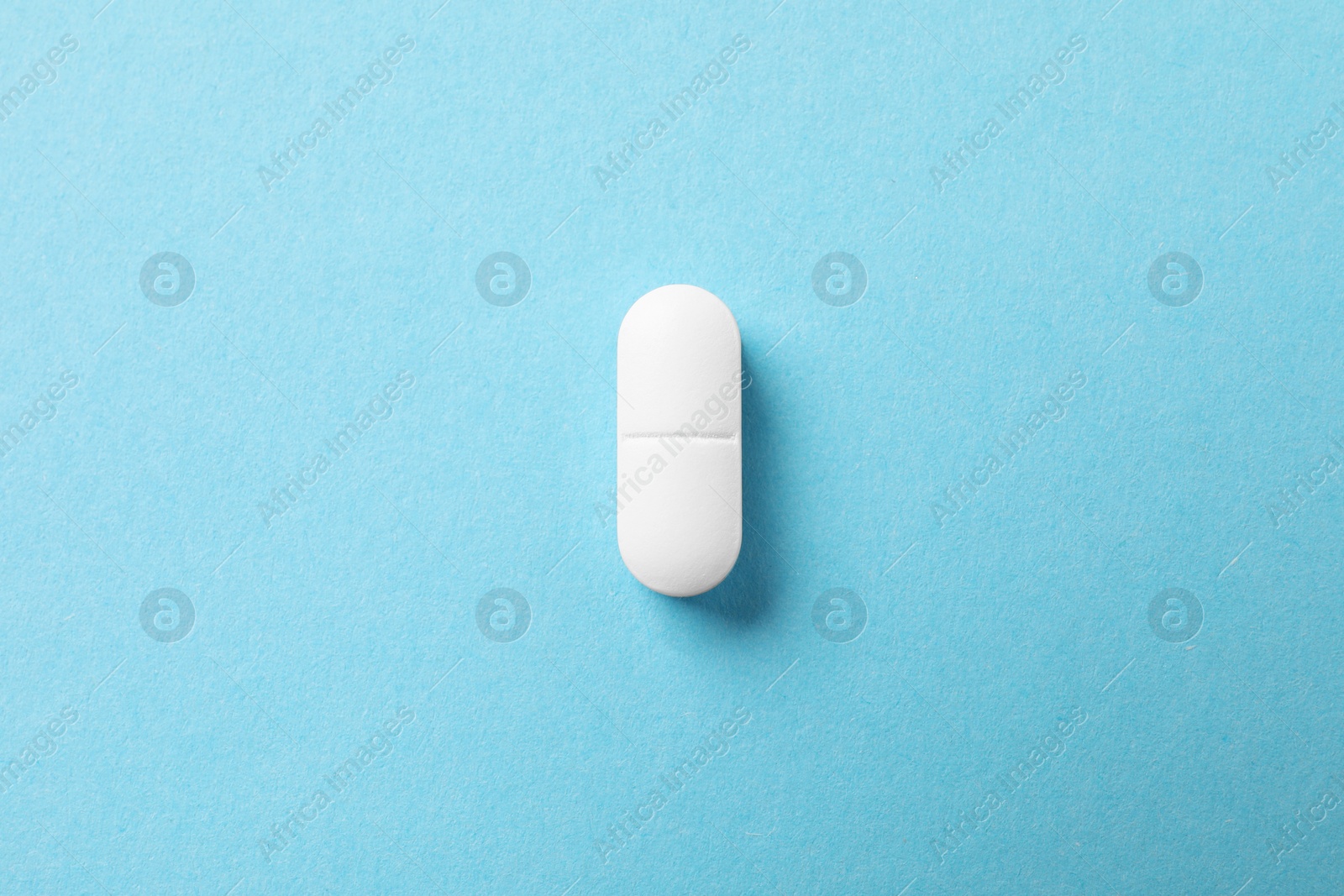 Photo of One white pill on light blue background, top view
