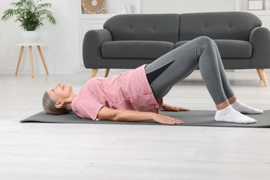 Photo of Senior woman in sportswear doing exercises on fitness mat at home