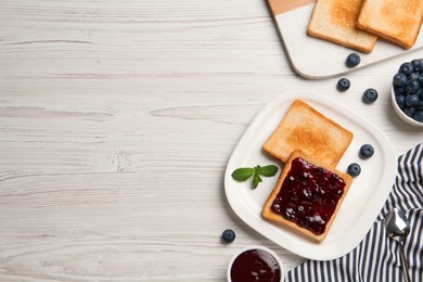 Photo of Toasts and blueberry jam served on white wooden table, flat lay. Space for text