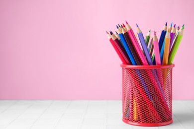 Photo of Many colorful pencils in holder on light table against pink background, space for text