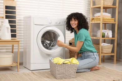 Happy woman with laundry near washing machine indoors