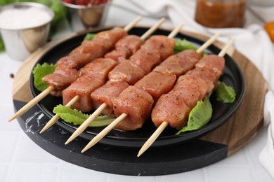 Photo of Wooden skewers with cut raw marinated meat on white tiled table, closeup
