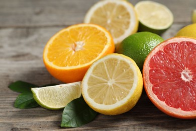 Different fresh citrus fruits and leaves on wooden table, closeup