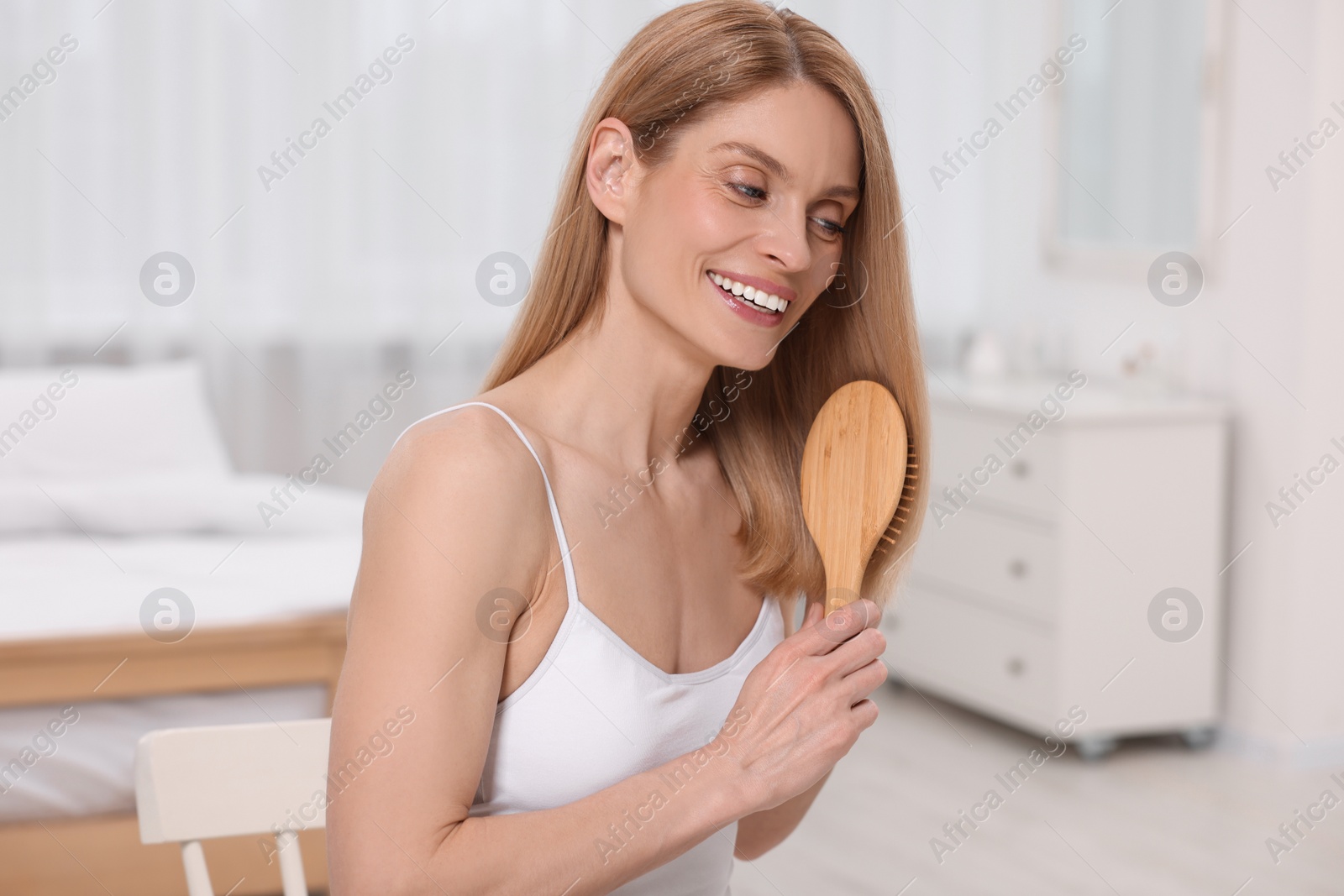 Photo of Beautiful happy woman brushing her hair in bedroom