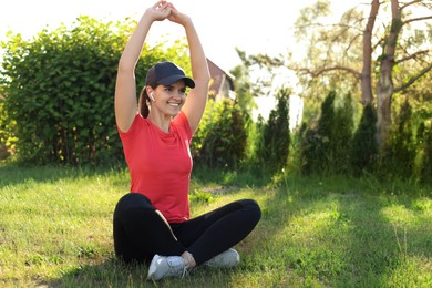 Photo of Young woman listening to music while doing morning exercise on green grass in park, space for text