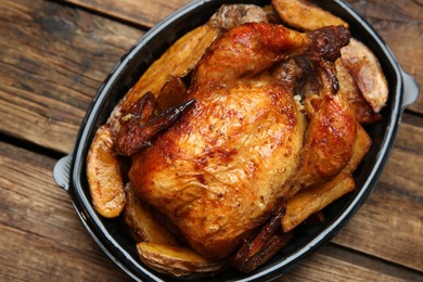 Photo of Delicious grilled whole chicken with potato in plastic container on wooden table, top view. Food delivery service