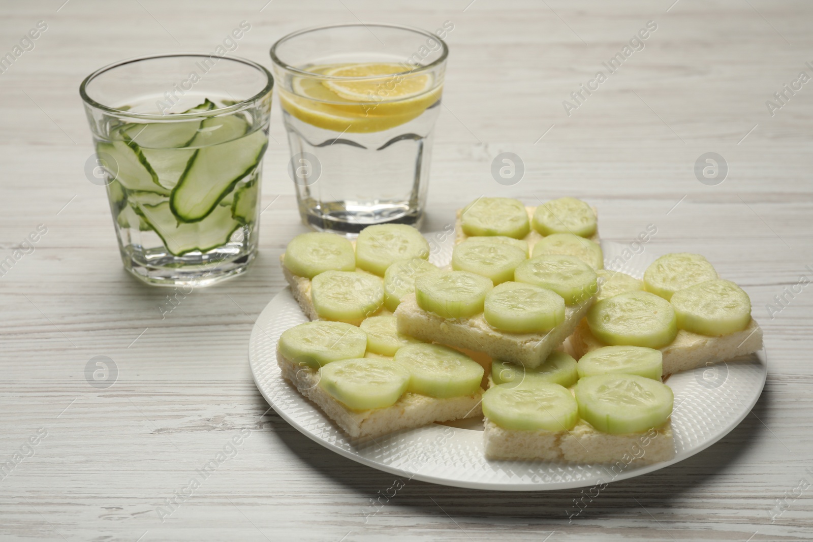 Photo of Tasty sandwiches with butter and cucumber served on white wooden table