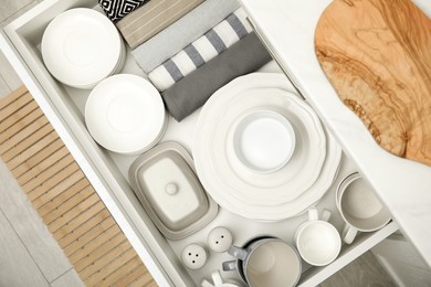 Photo of Open drawer of kitchen cabinet with different dishware and towels, top view