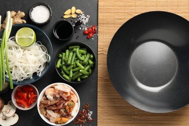 Flat lay composition with black wok, spices and products on dark textured table