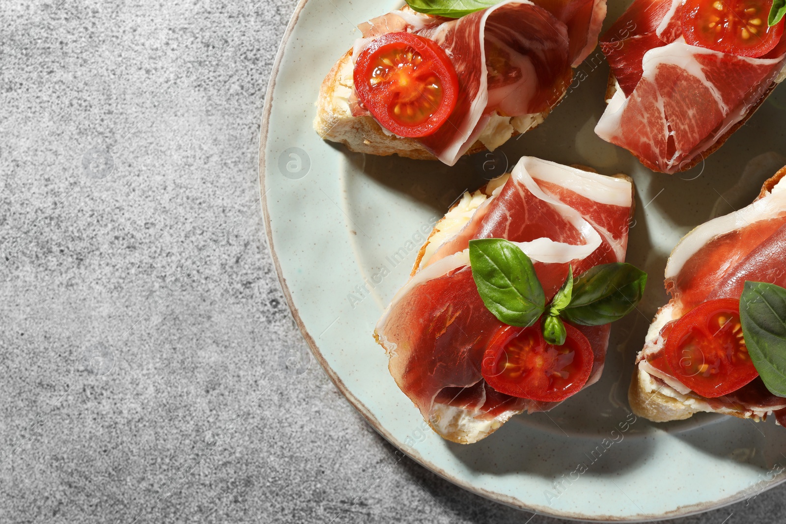 Photo of Tasty sandwiches with cured ham, basil and tomatoes on grey table, top view. Space for text