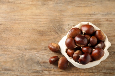 Photo of Fresh sweet edible chestnuts in sack on wooden table, flat lay. Space for text