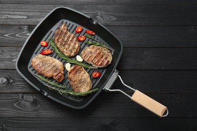 Grill pan with delicious pork steaks, garlic, chili pepper and rosemary on black wooden table, top view