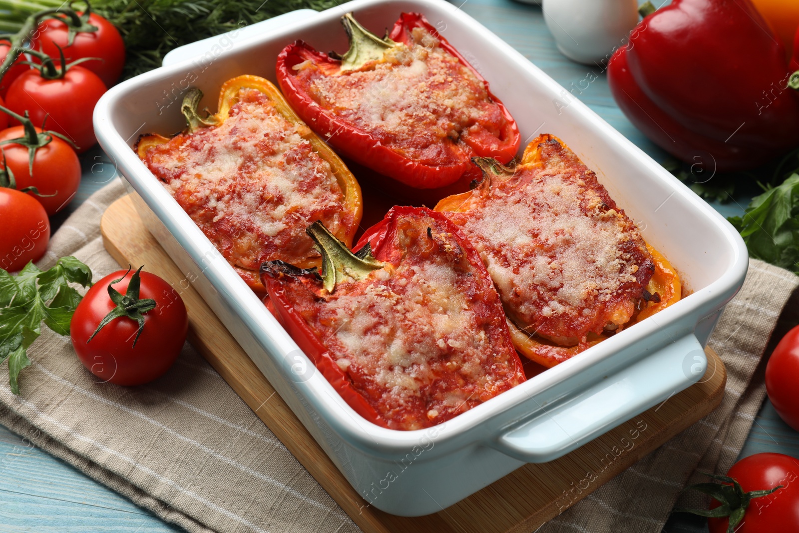 Photo of Tasty stuffed peppers in dish and ingredients on light blue wooden table