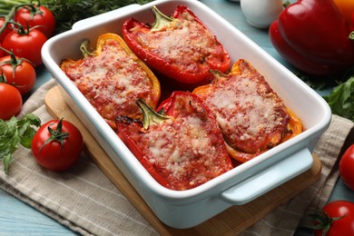 Photo of Tasty stuffed peppers in dish and ingredients on light blue wooden table