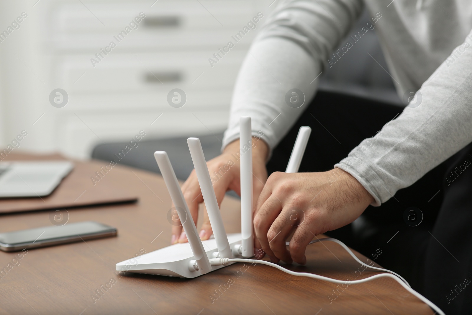 Photo of Man inserting cable into Wi-Fi router at wooden table indoors, closeup