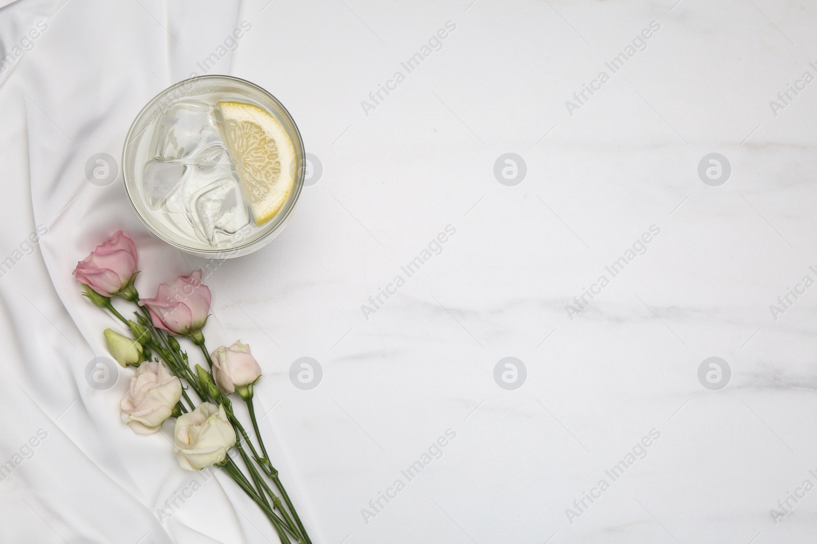 Photo of Refreshing drink, flowers and delicate fabric on white marble table, flat lay. Space for text