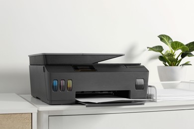 Photo of Modern printer with paper on chest of drawers indoors