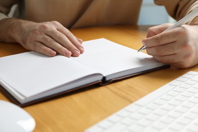 Photo of Left-handed man writing in notebook at wooden desk, closeup