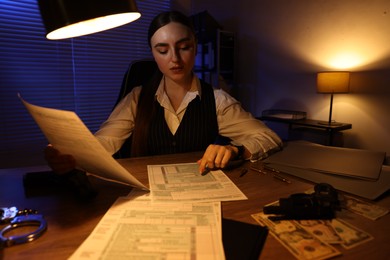 Photo of Professional detective working with documents in office at night