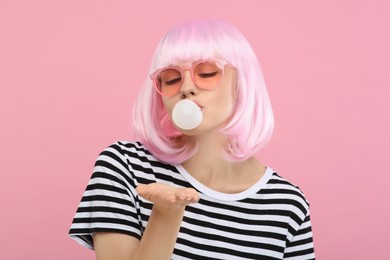 Beautiful woman in sunglasses blowing bubble gum on pink background
