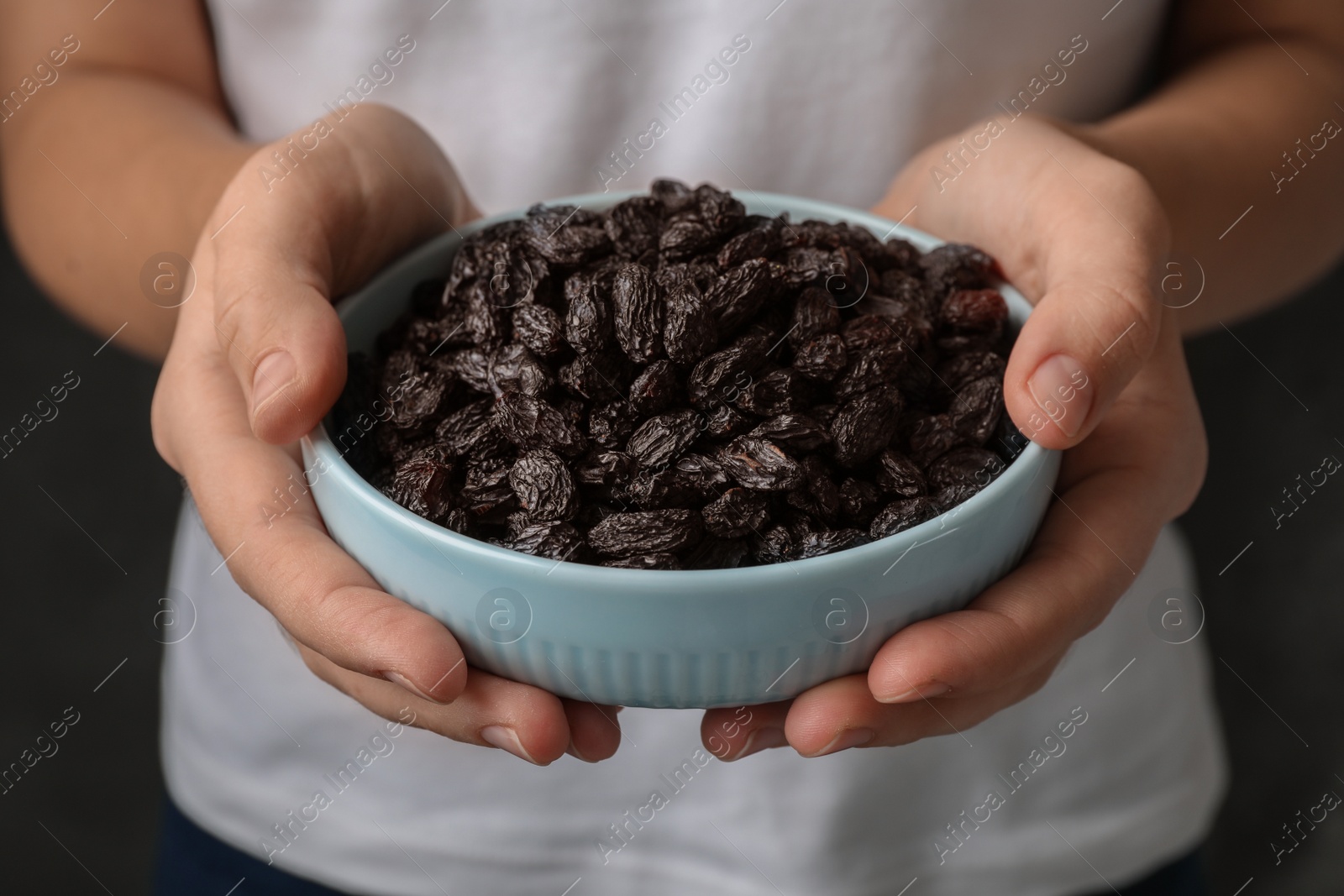 Photo of Woman holding bowl with raisins on black background, closeup