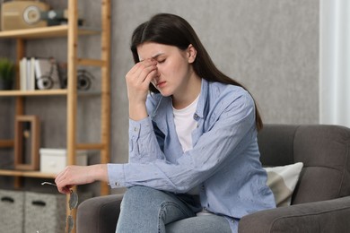 Overwhelmed woman with glasses sitting in armchair at home