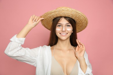 Teenage girl with sun protection cream on her face against pink background