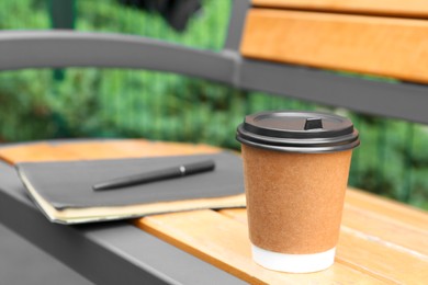 Cardboard cup with plastic lid on wooden bench outdoors, space for text. Coffee to go