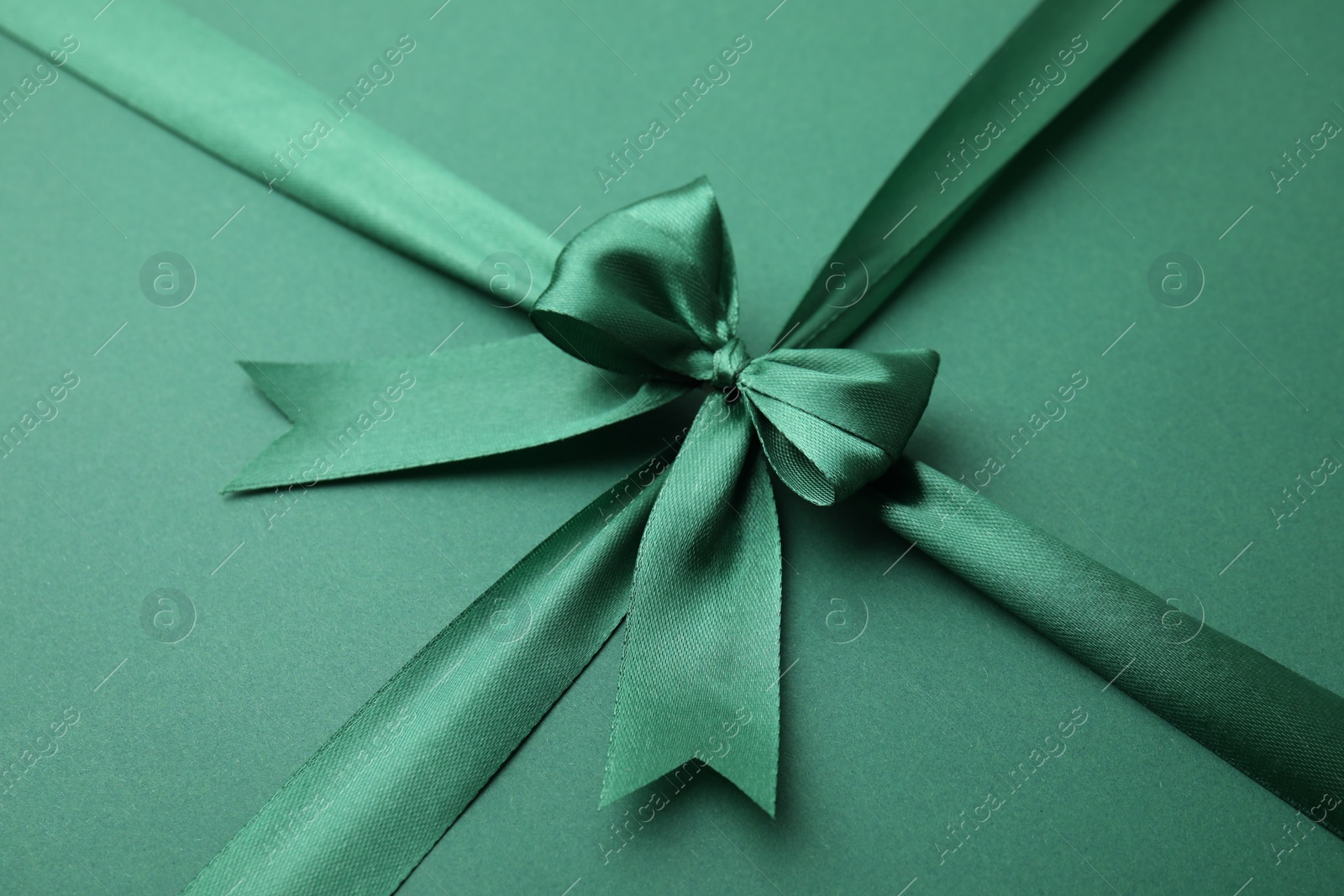 Photo of Bright satin ribbon with bow on green background